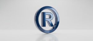 Símbolo de marca registrada em destaque no metal azul, representando a distintividade perante o INPI.