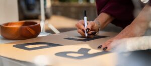 Mão escreve letra em papelão, criando tipologia de marca